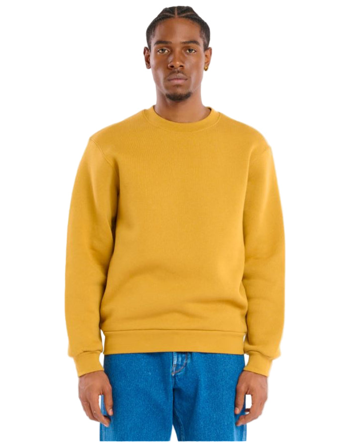 Man wearing a mustard yellow sweatshirt and blue jeans on a white background